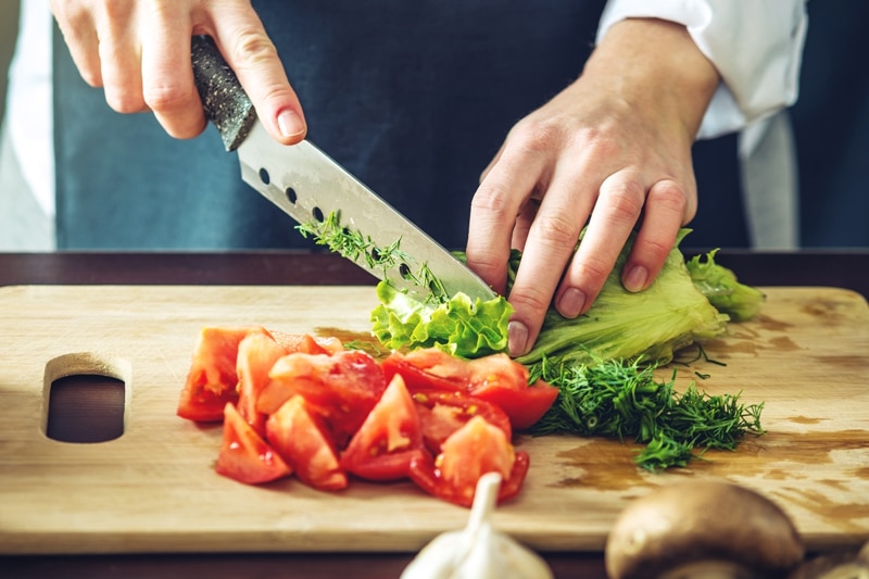 Person cutting lettuce and tomatoes on a cutting board