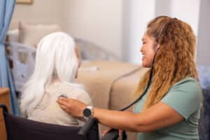 Staff member seated beside and speaking with a resident in a wheelchair.