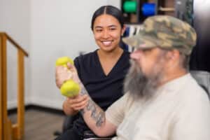Staff member smiling as a seated resident exercises with yellow hand weights.