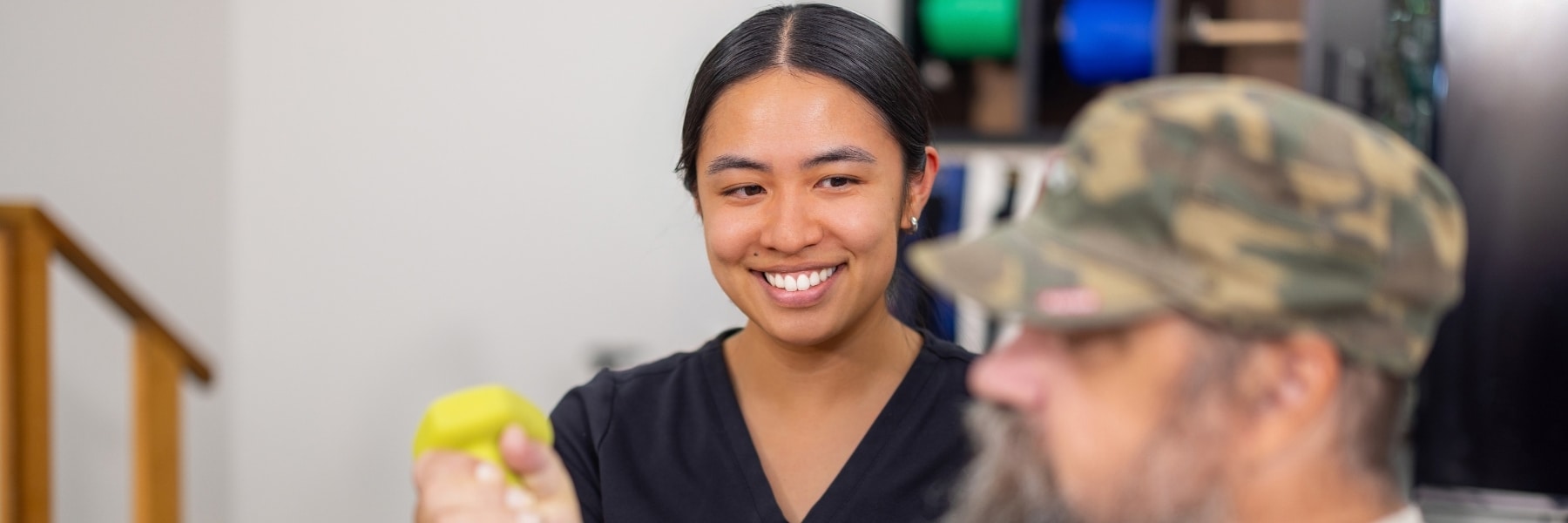 Staff member smiling beside a resident holding a yellow hand weight.